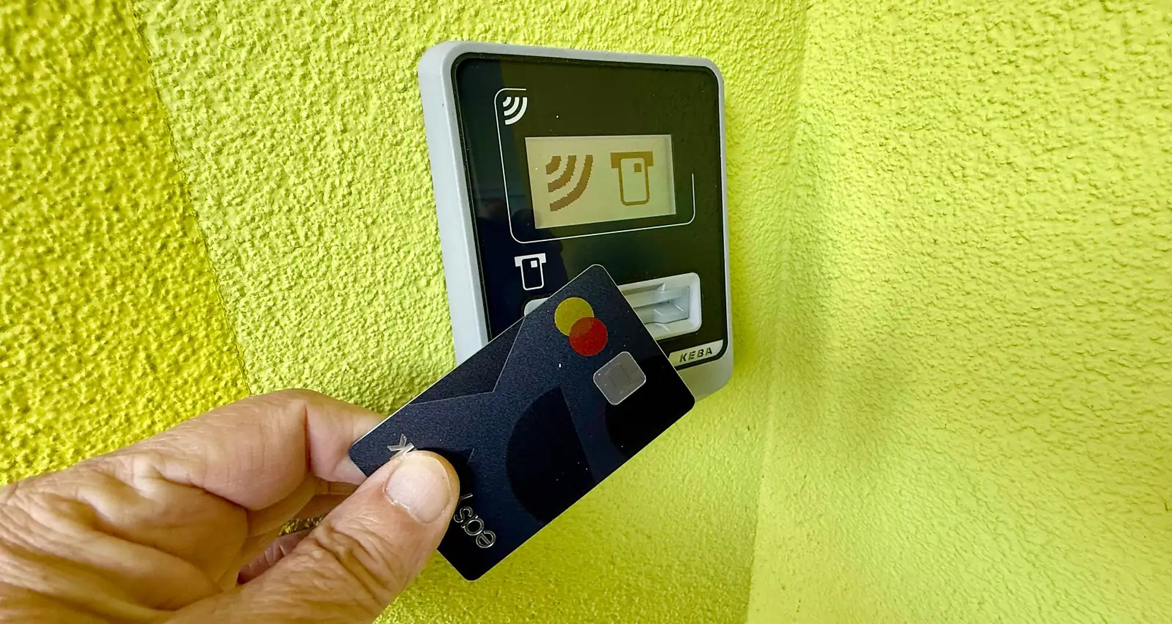 Eine Bankomatkarte wird an den Kartenleser an der grünen Hauswand gehalten.